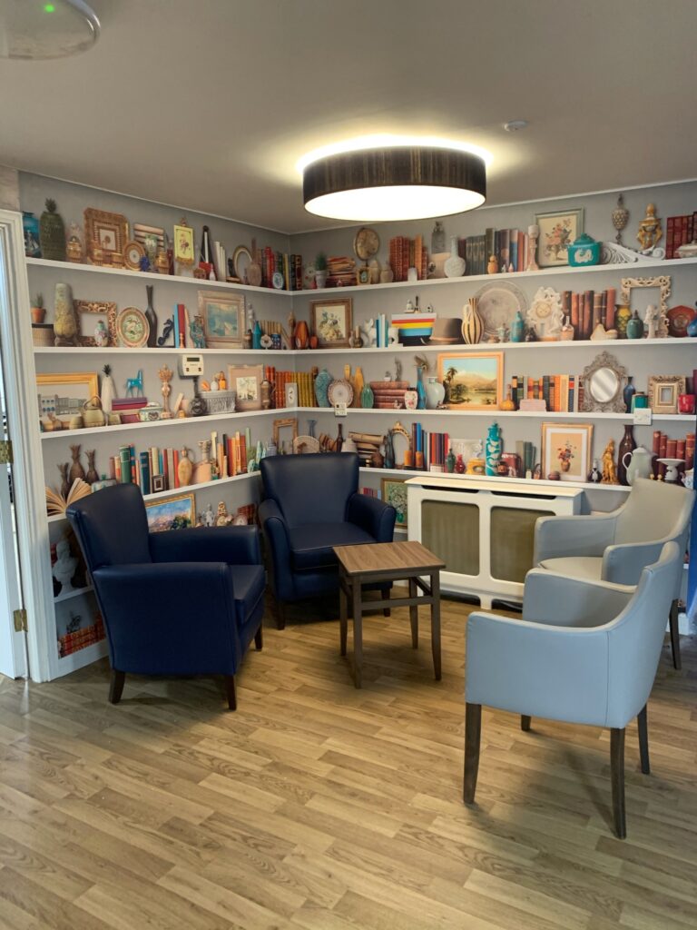 A reading corner featuring bright light, comfortable armchairs and distinctive shelf mural at The Glen care home